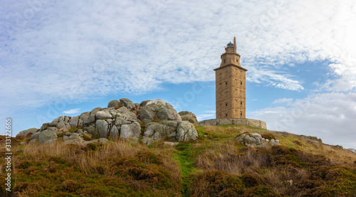 The lighthouse of La Coruna is the oldest in the world and is located in northern Spain on the Atlantic. The Hercules tower stands on a rock. The sky is blue with some clouds.