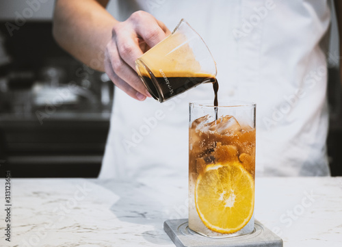 Refreshment summer drink. Barista making a cold brew espresso tonic with orange on the white stone table bar.