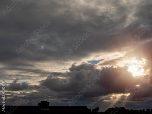 Dramatic sunset sky with sun rays and house roof silhouette.