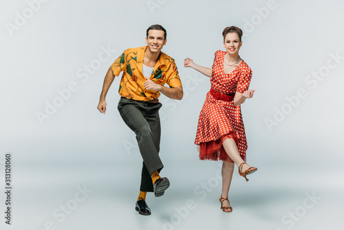Stylish couple looking at camera while dancing boogie-woogie on grey background