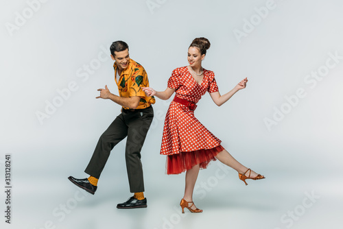 Young dancers holding hands while dancing boogie-woogie on grey background