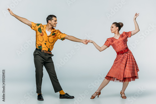 Obraz na płótnie elegant dancers holding hands while dancing boogie-woogie on grey background