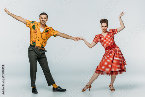 stylish dancers holding hands while dancing boogie-woogie on grey background