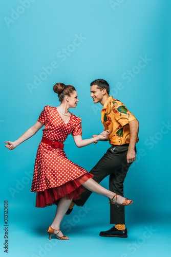 smiling dancers looking at each other while dancing boogie-woogie on blue background