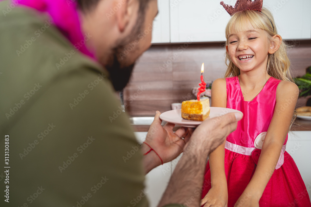 Young man giving piece of cake to joyful daughter Young man giving piece of cake to joyful daughter