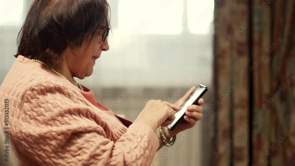 Senior Woman Using Smartphone For Social Networks And Browsing In Internet.Grandmother In Glasses Scrolling On Screen On Cellphone.Senior Woman Using Mobile Phone.Mature Woman Holding Mobile Phone. Senior Woman Using Smartphone For Social Networks And Browsing In Internet.Grandmother In Glasses Scrolling On Screen On Cellphone.Senior Woman Using Mobile Phone.Mature Woman Holding Mobile Phone.