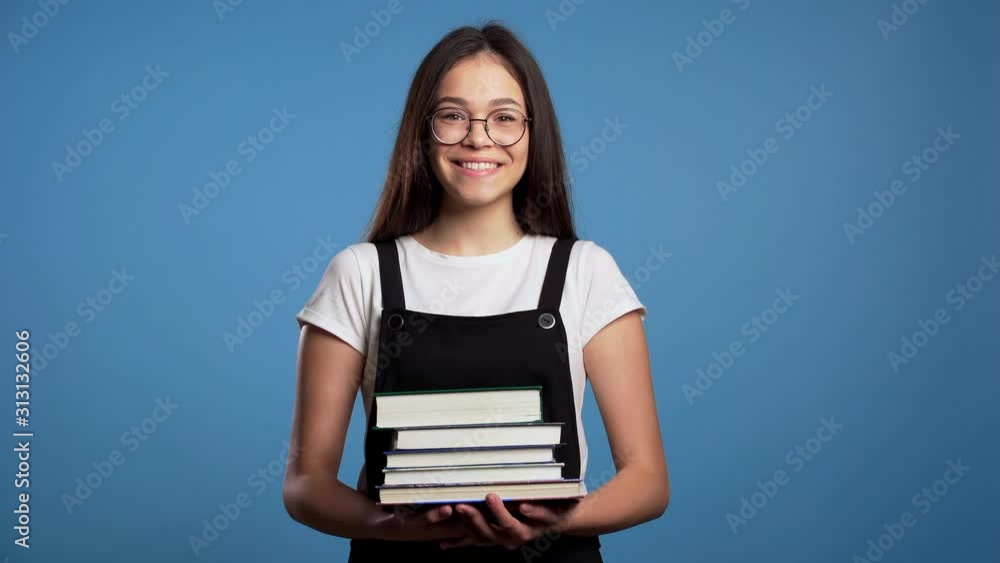 Asian student girl on blue background in the studio holds stack of university books from library. Woman smiles, she is happy to graduate. Asian student girl on blue background in the studio holds stack of university books from library. Woman smiles, she is happy to graduate.