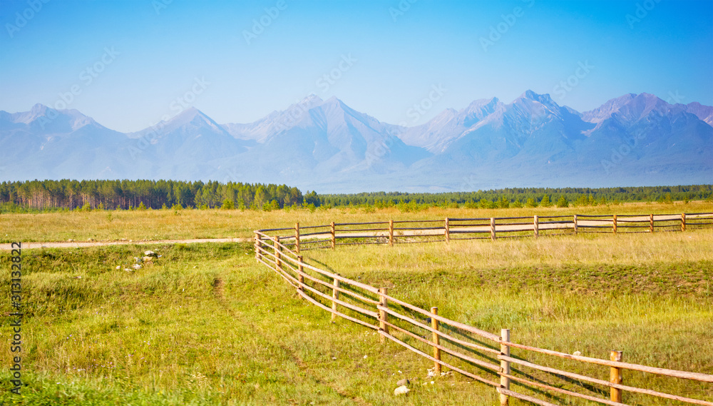 Beautiful landscape with wooden fence, pasture, forest and mountains. The Tunka valley, Buryatia, Russia.
