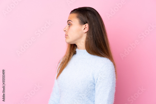 Teenager girl with blue sweater over isolated pink background looking to the side © luismolinero