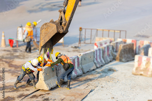 Many workers wear safety suits helped to lift and arrange the cement concrete barriers by excavator In harmony and actively on the road photo