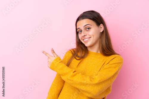 Teenager girl with yellow sweater over isolated pink background pointing back