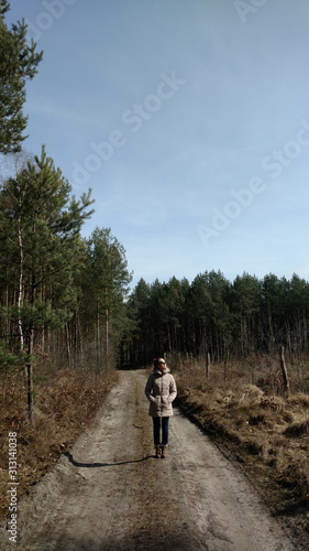 Young woman walking away alone on a forest path wearing sunglasses. Early spring time in march.