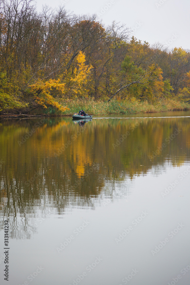 Fototapeta premium The boat floats by the river through the autumn forest.