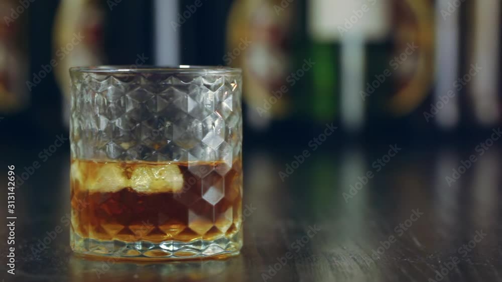 Glass with whiskey and ice. Whiskey pouring in the glass from the bottle. With ice cubes. Glass with whiskey and ice. Whiskey pouring in the glass from the bottle. With ice cubes.