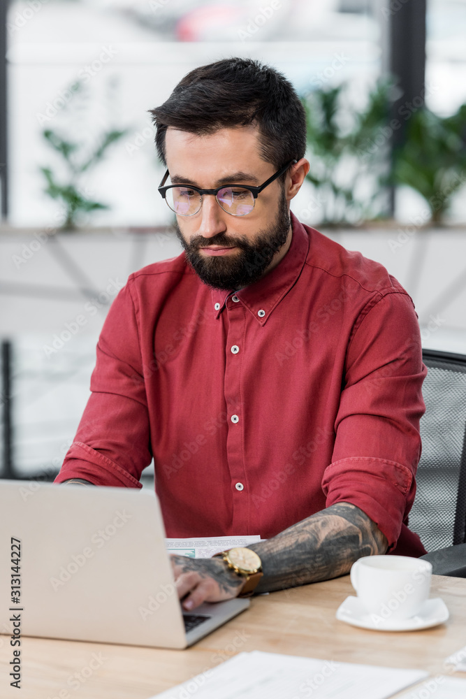 handsome account manager sitting at table and using laptop