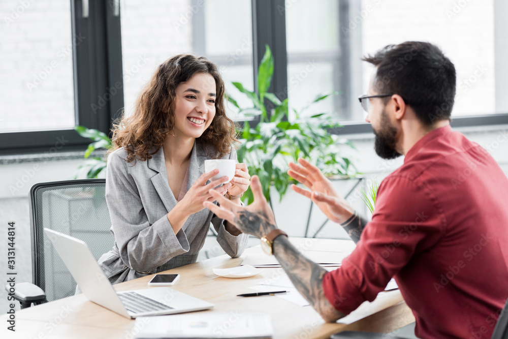 smiling account manager holding cup and talking with colleague smiling account manager holding cup and talking with colleague