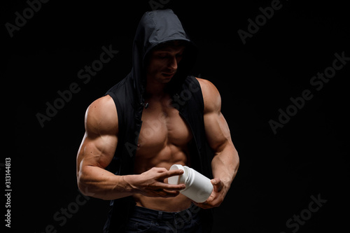 Muscular bodybuilder with jar of protein on a dark background. Sports nutrition. Bodybuilding nutrition supplements, sport, workout, healthy lifestyle concept.