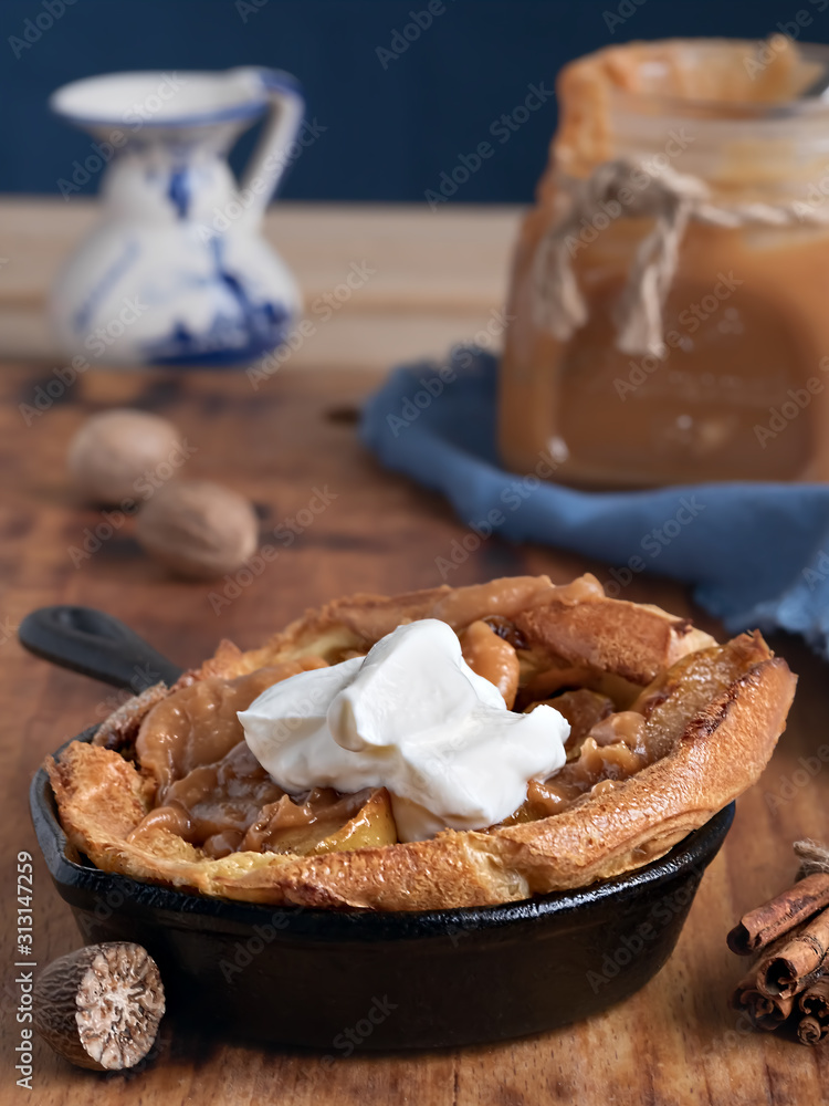 Homemade apple pie with caramel sauce and cream on a wooden table. Close-up, selective focus on the cream. Near a jar of caramel, milk and spices. Tasty dessert. Homemade apple pie with caramel sauce and cream on a wooden table. Close-up, selective focus on the cream. Near a jar of caramel, milk and spices. Tasty dessert.