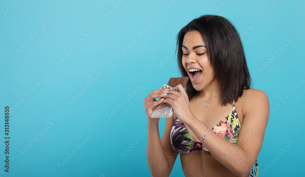 Portrait of a smiling young african woman eating chocolate bar isolated over blue background Portrait of a smiling young african woman eating chocolate bar isolated over blue background