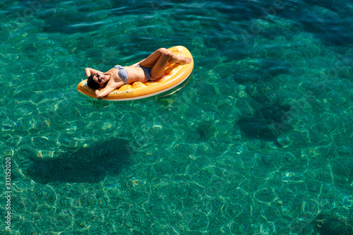 Slim young woman in bikini and sunglasses on the air mattress floats in the open sea. © Nikolay