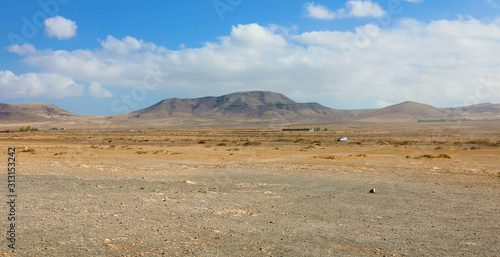 Dry soil under white clouds and blue sky with moutains on the background panoramic view on Fuerteventura Island