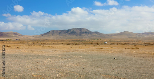 Konstfotografi Dry soil under white clouds and blue sky with moutains on the background panoram