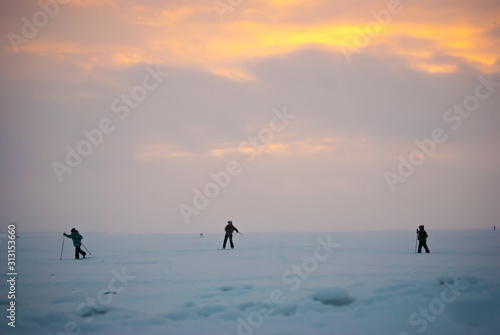 A lonely family of skiers in the distance riding on a frozen lake at sunset surrounded by snow