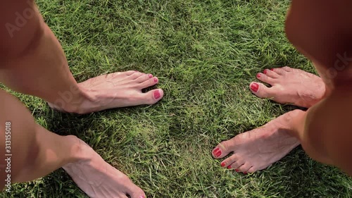 Two pairs of female feet,with pink and red nails, stand opposite each other on the green grass,and wiggle their fingers,top view.