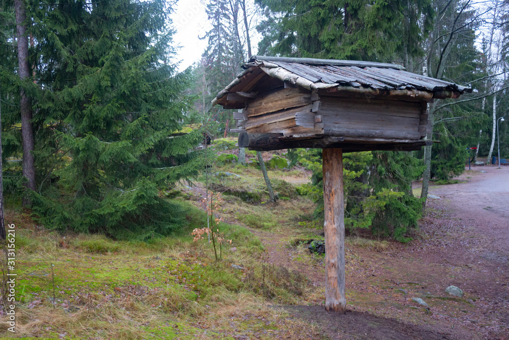 An old authentic little wooden house on top of a log above the ground for an 18th-century hunter in the midst of a gloomy autumn pine forest on the island of Seurasaari in Helsinki, Finland. An old authentic little wooden house on top of a log above the ground for an 18th-century hunter in the midst of a gloomy autumn pine forest on the island of Seurasaari in Helsinki, Finland.