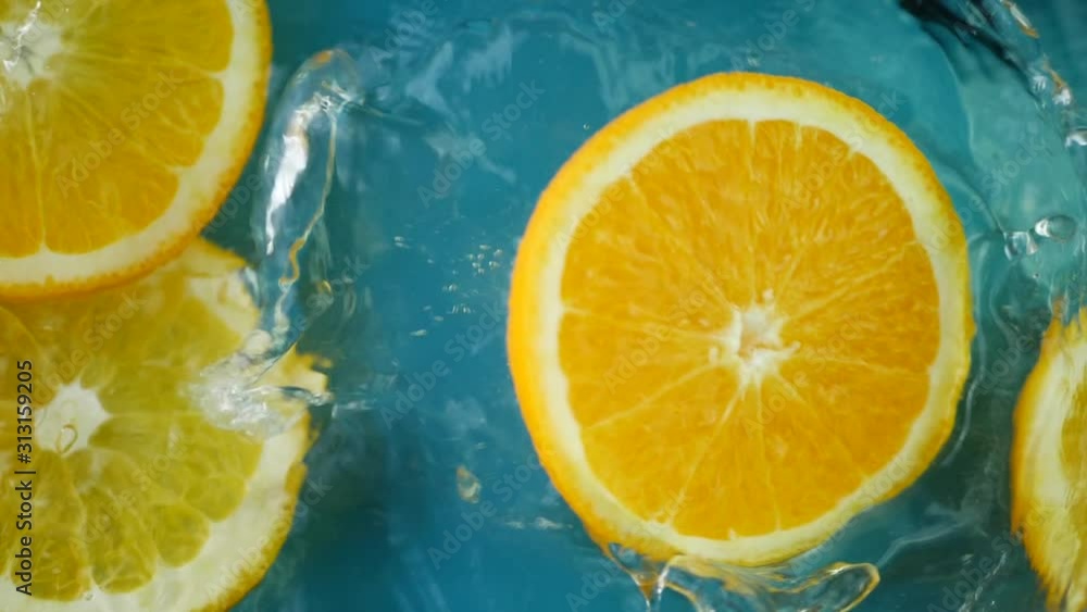 Fresh oranges falling in water juice with lot of huge splashes on blue background. Summer cold drink and fresh food concept Fresh oranges falling in water juice with lot of huge splashes on blue background. Summer cold drink and fresh food concept