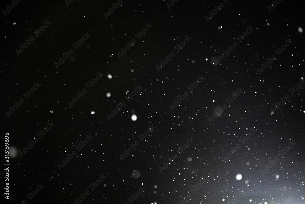 Snow and bokeh in the light of a lantern on a black background