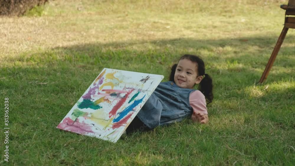 Portrait of little girl sit on grass with painting then fall back and smile, she look happy in park or garden. Portrait of little girl sit on grass with painting then fall back and smile, she look happy in park or garden.