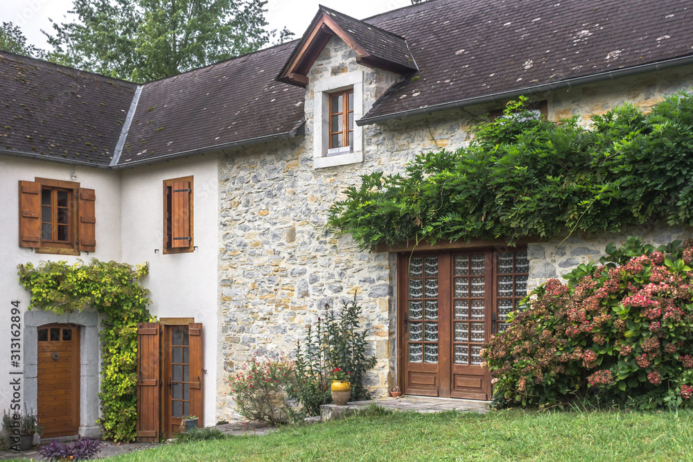 A private house. Country mansion. Old building. Closed entrance to the house. French village. Stone facade. Medieval architecture. Rural cottage. Stone wall. Landscaping in the yard.
