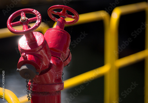 an industrial red metal standpipe fire hydrant by a yellow barrier.