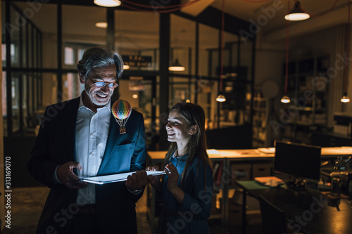 Happy senior businessman and girl with hot-air balloon and shining tablet in office photo