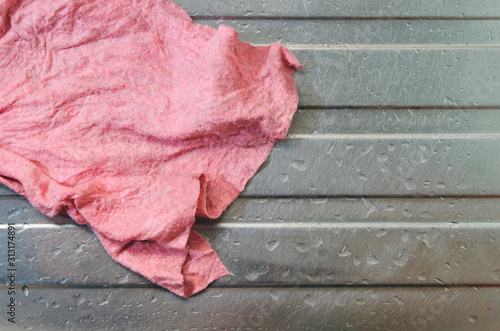 Single wet dirty used pink dishcloth (washcloth). Placed on top of a steel kitchen sink with water droplets all around. No people, real raw shot. Copy space. Concept for unhealthy and germs growth
