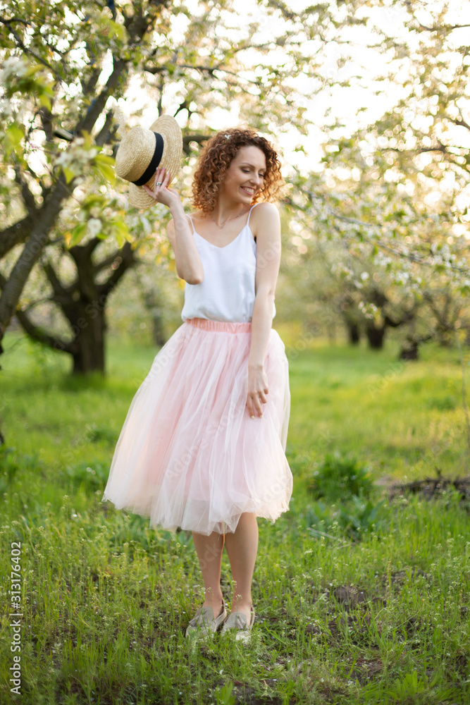 Young attractive woman with curly hair walking in a green flowered garden. Spring romantic mood Young attractive woman with curly hair walking in a green flowered garden. Spring romantic mood