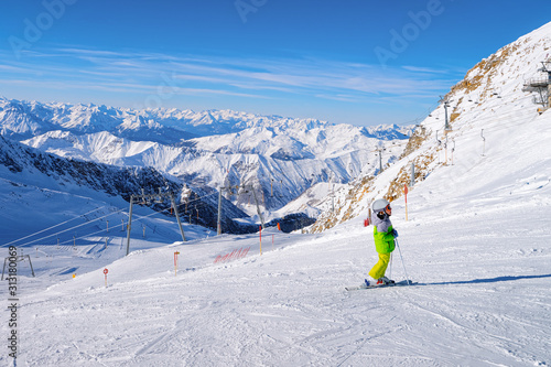 Child Skier skiing in Hintertux Glacier in Tyrol in Mayrhofen in Austria, winter Alps. Kid Ski at Hintertuxer Gletscher in Alpine mountains with white snow and blue sky. Austrian snowy slopes
