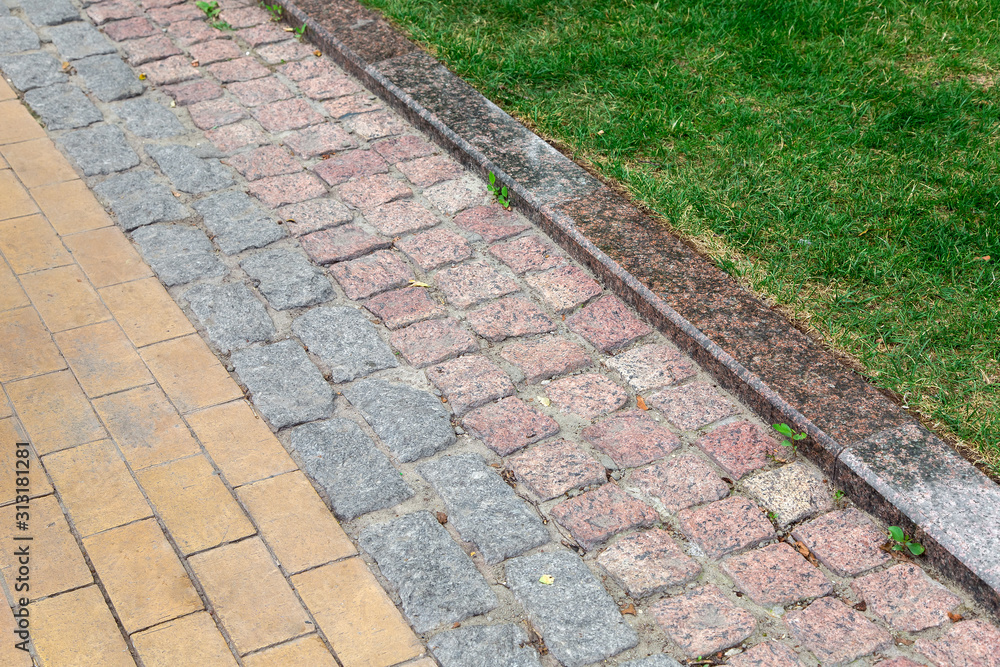 a footpath made of tiles of different types of stone and a granite curb in the park with a green trova in the park.