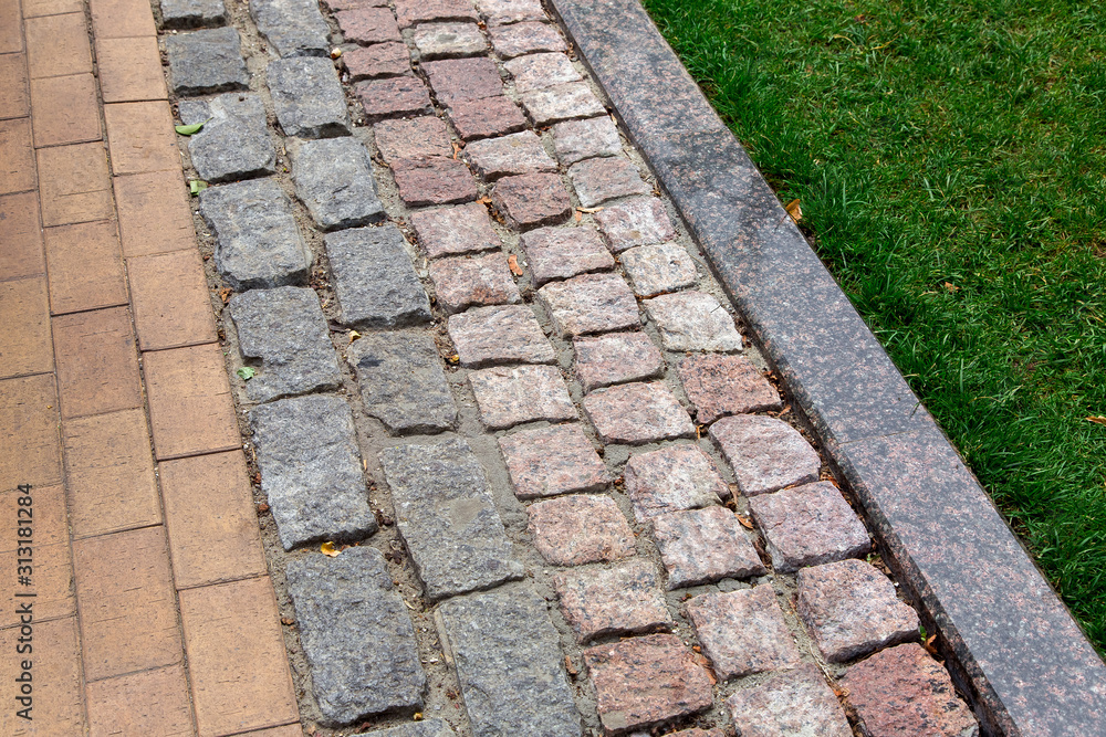 a pedestrian pavement made of stone and granite tiles with a curb near a green lawn in the park, close up.