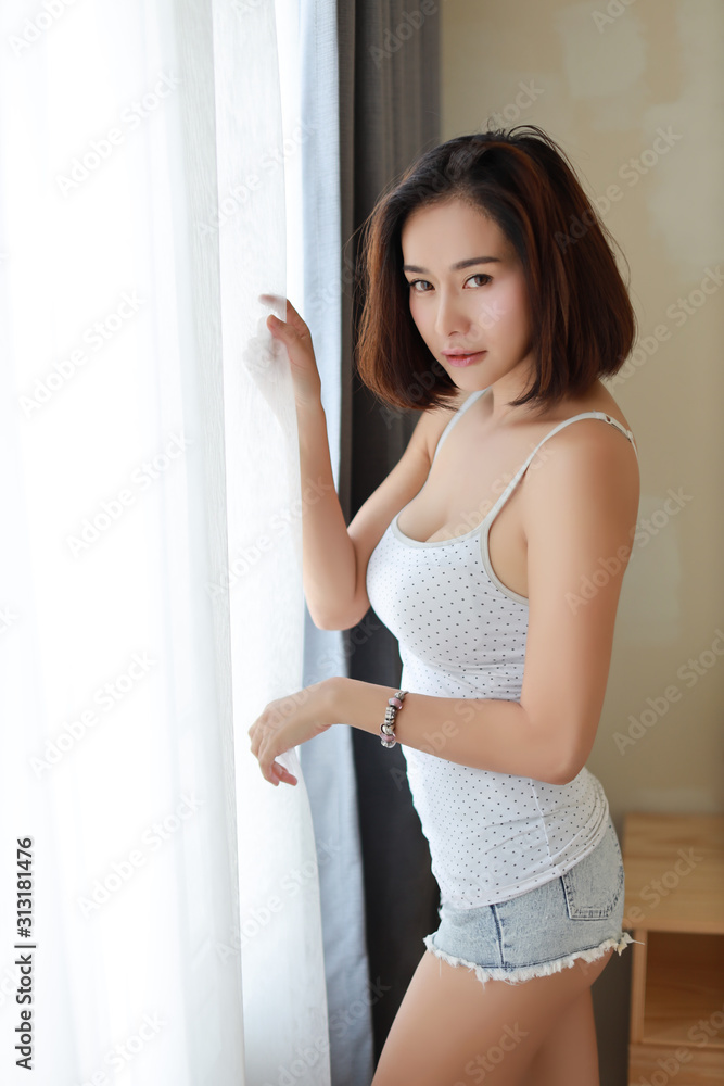 good shape and healthy asian young woman wake up in the morning at sunrise. She standing and opening curtain at the window in bedroom good shape and healthy asian young woman wake up in the morning at sunrise. She standing and opening curtain at the window in bedroom