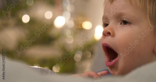 Portrait of tired yawing toddler boy falling asleep, Christmas celebrations, shallow depth of field photo