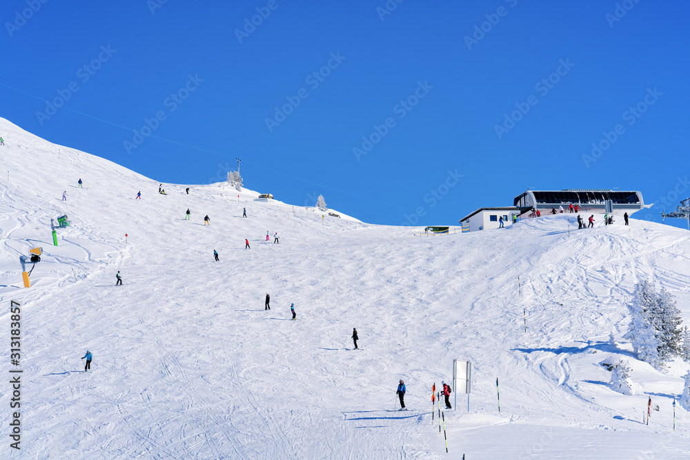 Skiers skiing at Zillertal Arena ski resort in Tyrol in Mayrhofen in Austria in winter Alps. Alpine mountains with white snow and blue sky. Downhill peaks at Austrian snowy slopes.