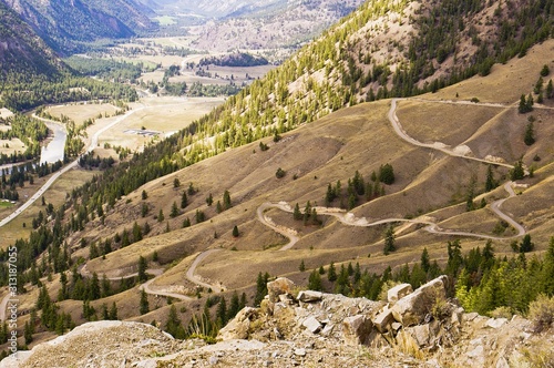 A winding mountain road leading down to a valley photo