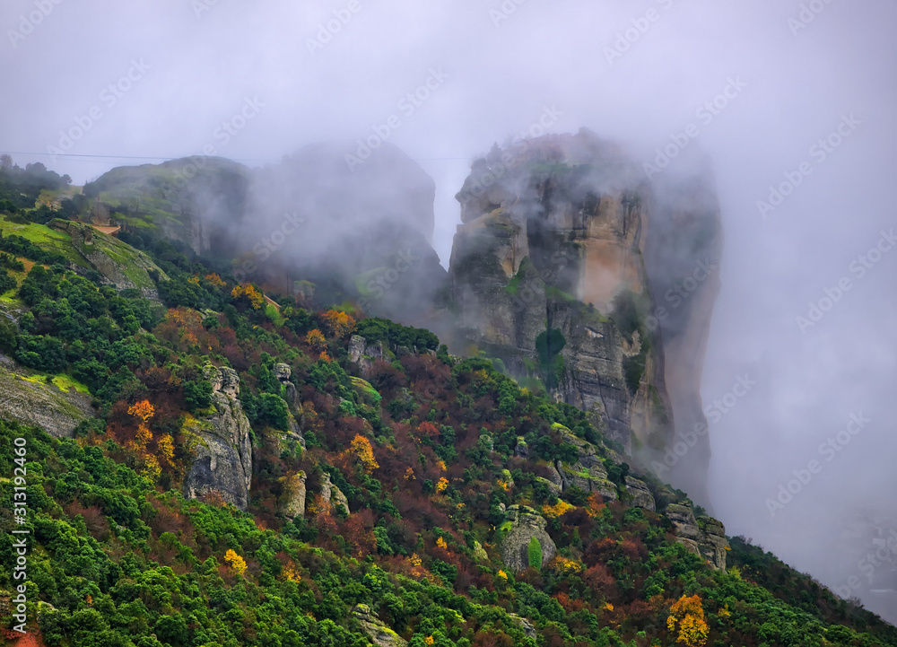 Fototapeta premium Meteora, Greece, winter dramatic landscape with heavy clouds and foggy mountains. Vibrant colorful nature.