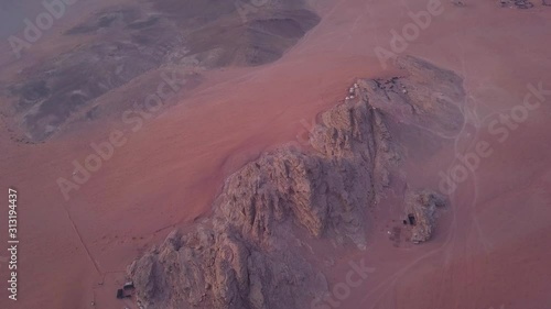 High Altitude Aerial Shot that Pans up from Desert Below to Reveal Tall Sandstone Cliffs of Wadi Rum in Jordan photo