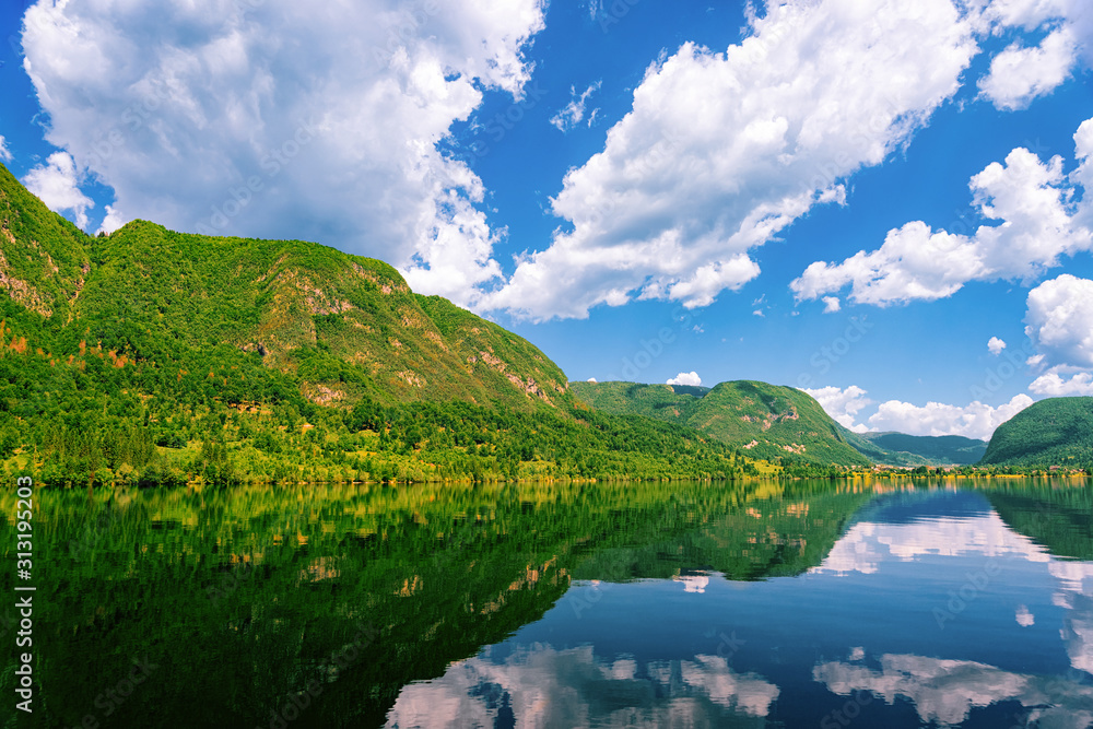 Scenery on Bohinj Lake of Slovenia. Nature in Slovenija. View of green forest and blue water. Beautiful landscape in summer. Alpine Travel destination. Julian Alps mountains on scenic background Scenery on Bohinj Lake of Slovenia. Nature in Slovenija. View of green forest and blue water. Beautiful landscape in summer. Alpine Travel destination. Julian Alps mountains on scenic background