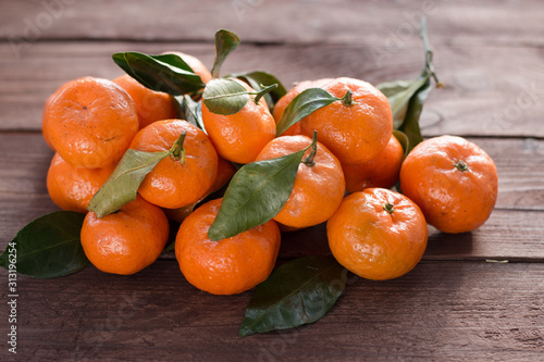 Ripe orange tangerines with green leaves on a dark wooden background. Fresh healthy food. Winter fruits. Organic food.