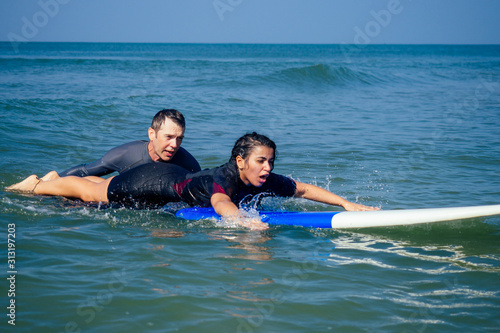 man instructor demonstrating how to paddle in the water by hands on surfboard to indian woman in surf class in Goa sea © yurakrasil