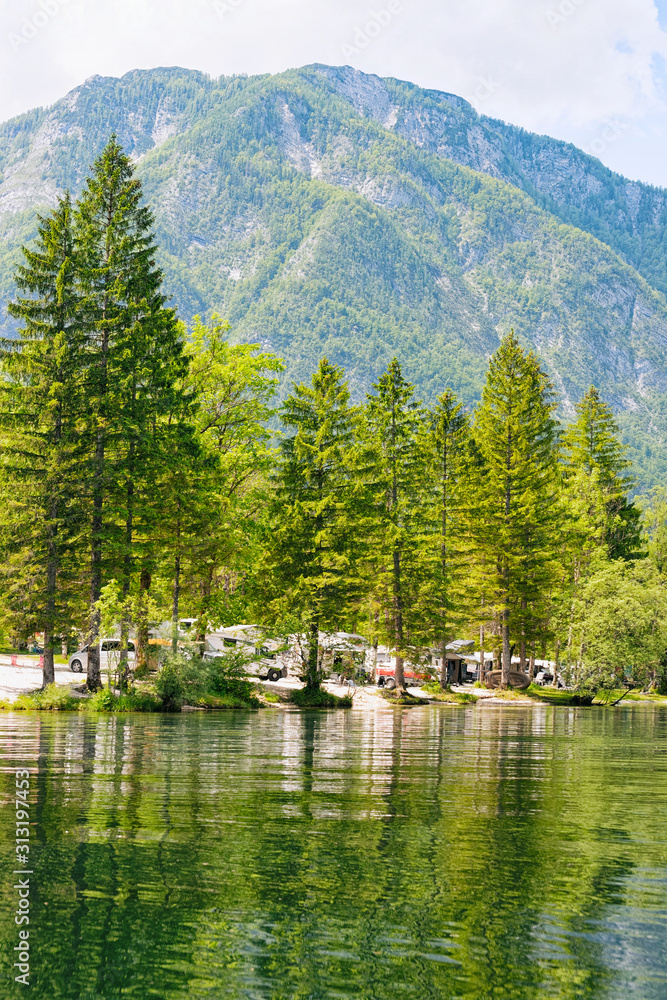 Scenery with camping of RV caravan trailers at Bohinj Lake in Slovenia. Nature and camper motorhomes in Slovenija. View of motor home van and green forest. Landscape in summer. Alpine Alps mountains